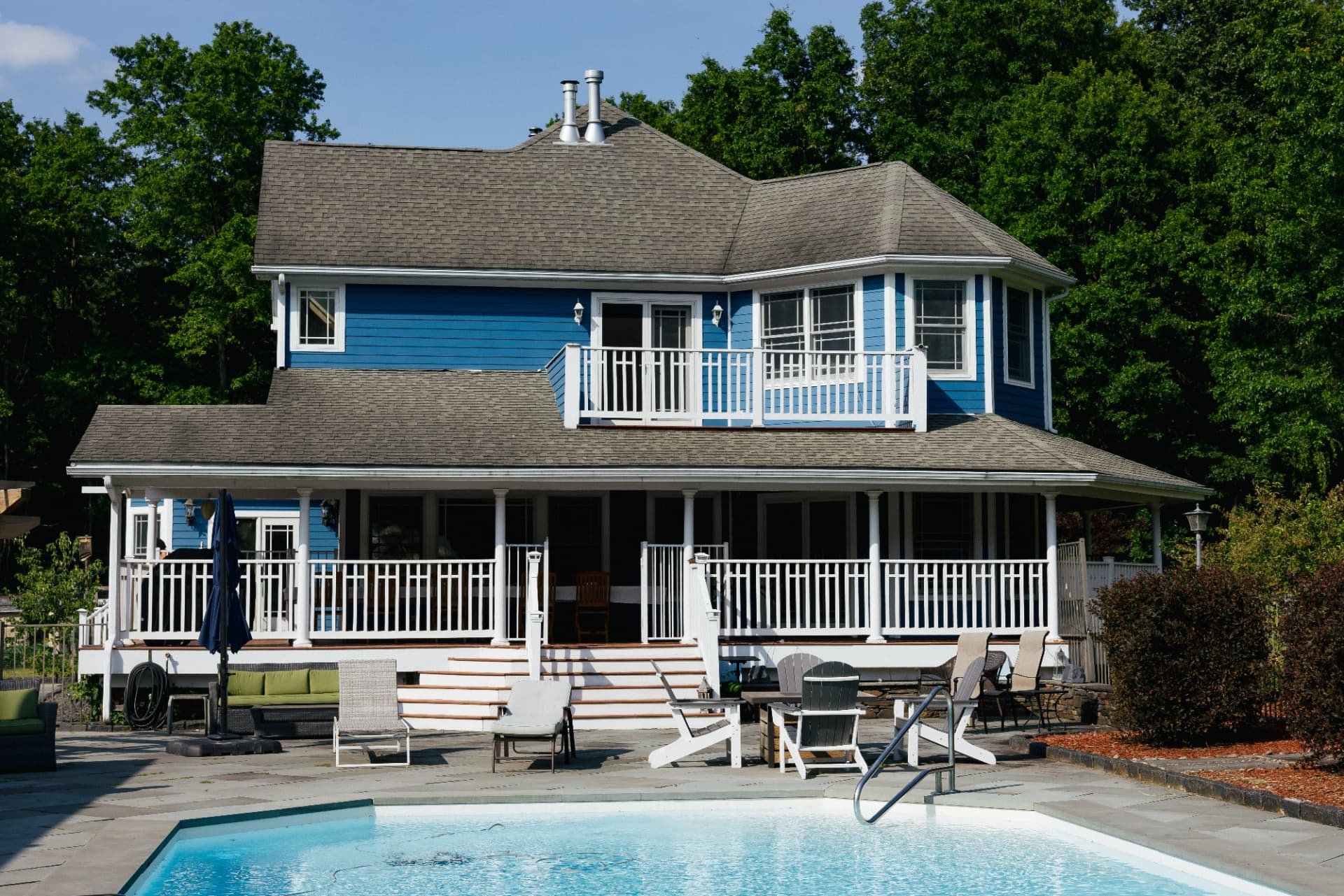 The blue house and wraparound porch seen across the pool