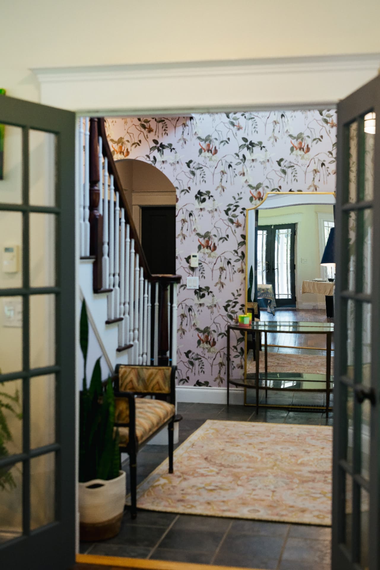 Entry hall with floral wallpaper, staircase and gold mirror