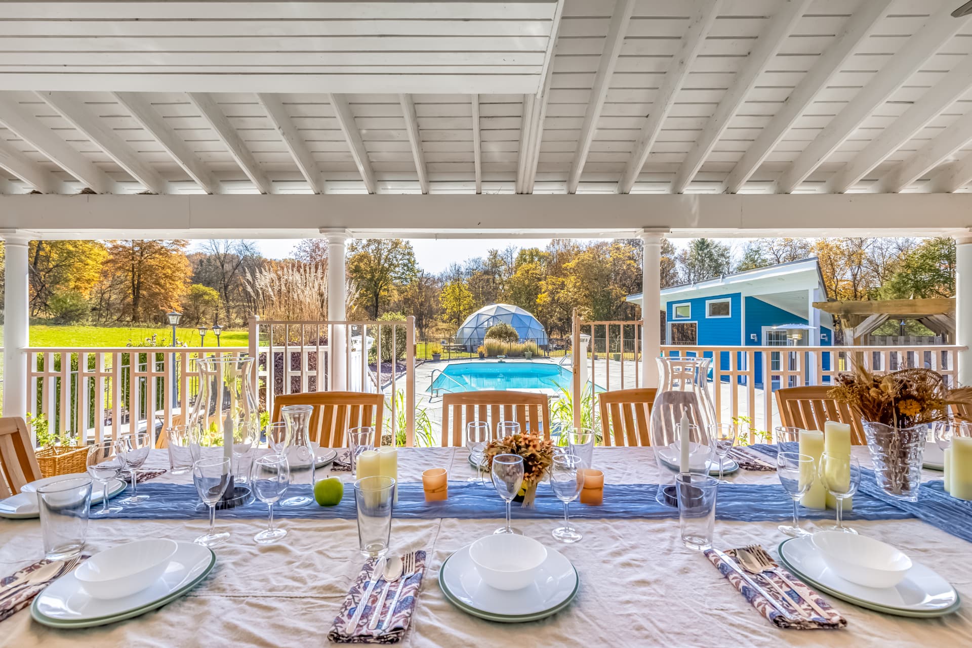 Long table set on the covered porch overlooking the pool and autumn treeline