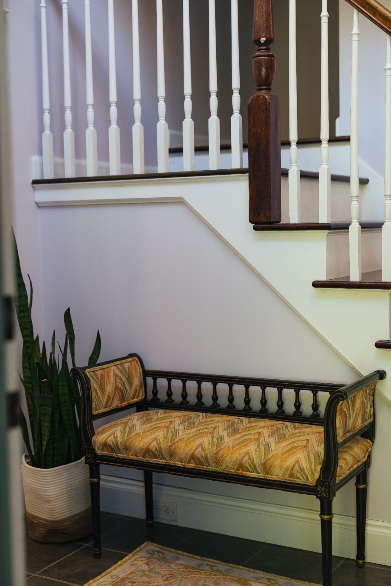 Antique upholstered bench beneath the staircase in the entry