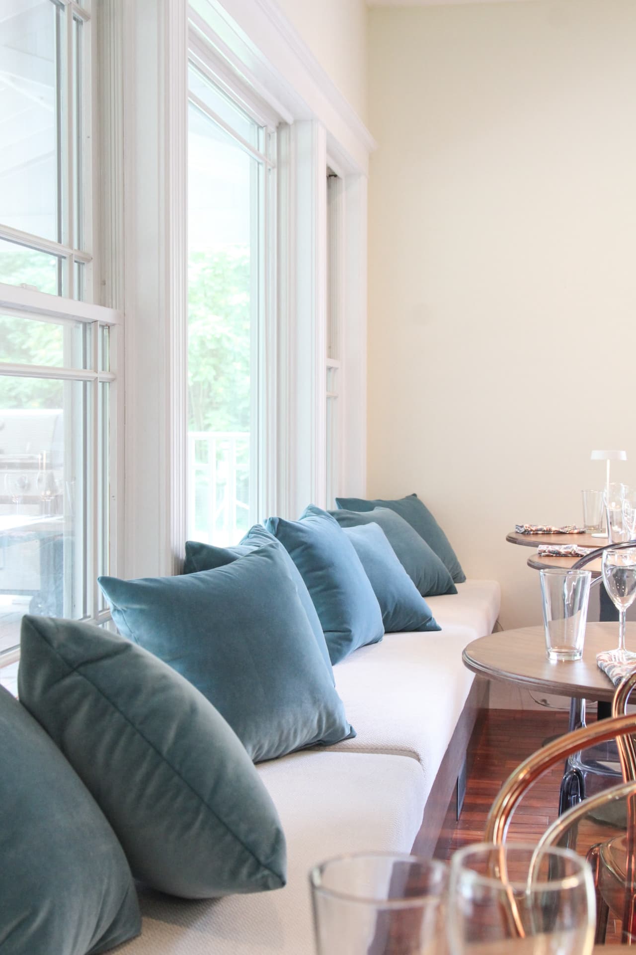 Cushioned window bench with velvet pillows beside dining tables