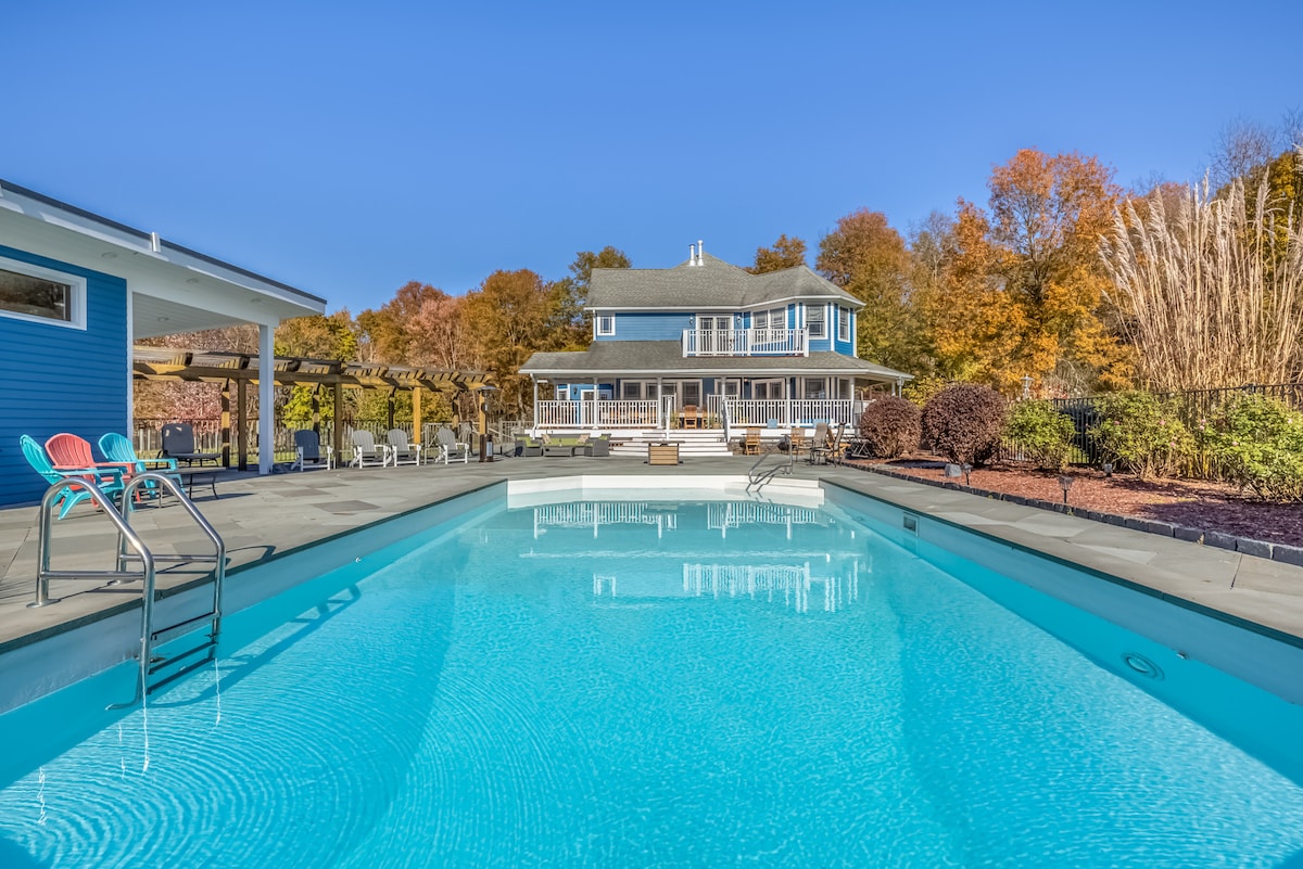 The pool at Thee Wild Lux looking back at the historic blue estate house — fall foliage, slate terrace, Hudson Valley