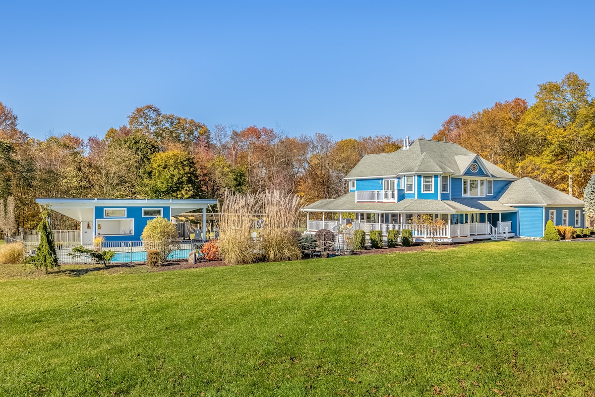 Thee Wild Lux estate from the front lawn — blue Victorian house, pool house, green lawn, fall foliage