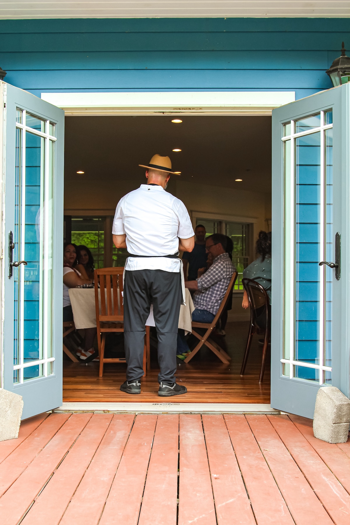 Private chef entering the estate dining room at Thee Wild Lux — guests seated, blue French doors, intimate event