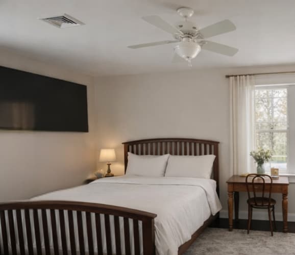 The Garden Room at Thee Wild Lux — cream walls, dark walnut bed frame, white linens, ceiling fan, garden window view
